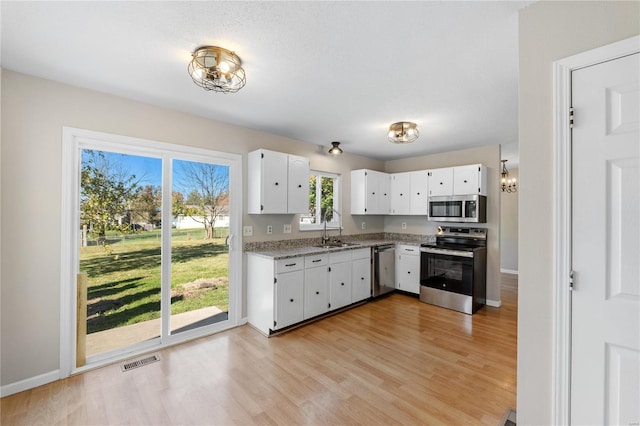 kitchen featuring sink, light wood-type flooring, light stone counters, white cabinetry, and stainless steel appliances