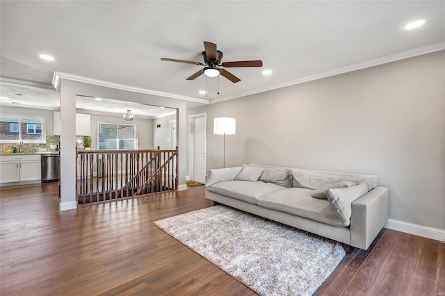 living room featuring dark wood-type flooring, ornamental molding, and ceiling fan with notable chandelier