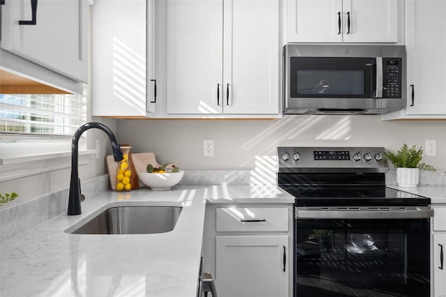 kitchen featuring stainless steel appliances, light stone countertops, white cabinets, and sink