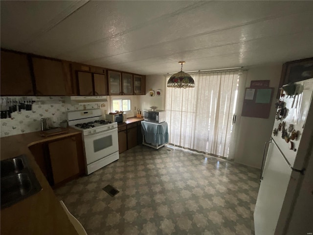 kitchen featuring decorative light fixtures, a textured ceiling, exhaust hood, sink, and white appliances