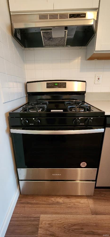 kitchen with white cabinetry, gas range, hardwood / wood-style floors, decorative backsplash, and exhaust hood