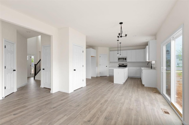 kitchen with appliances with stainless steel finishes, light hardwood / wood-style flooring, a center island, white cabinets, and pendant lighting