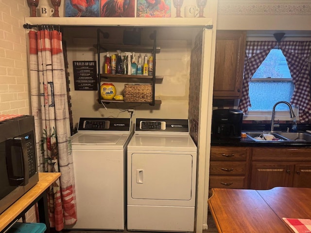 laundry room featuring washing machine and clothes dryer, brick wall, and sink