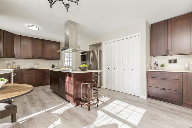 kitchen with a kitchen island, a breakfast bar, island exhaust hood, light hardwood / wood-style flooring, and appliances with stainless steel finishes