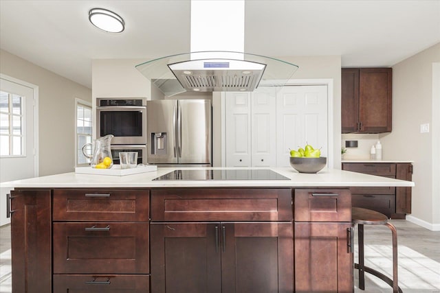 kitchen with a breakfast bar, island range hood, a center island, and stainless steel appliances