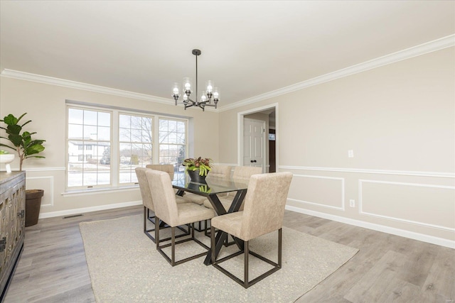 dining room with light hardwood / wood-style floors, ornamental molding, and an inviting chandelier