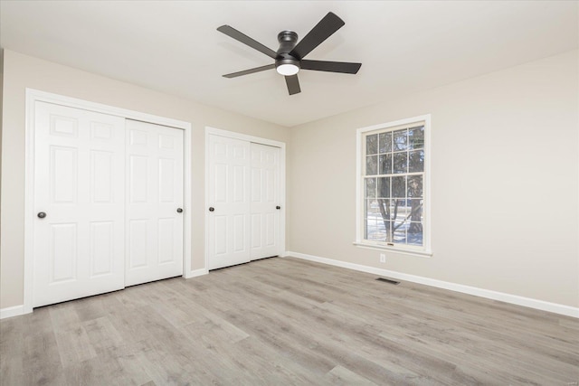 unfurnished bedroom featuring ceiling fan, light wood-type flooring, and two closets