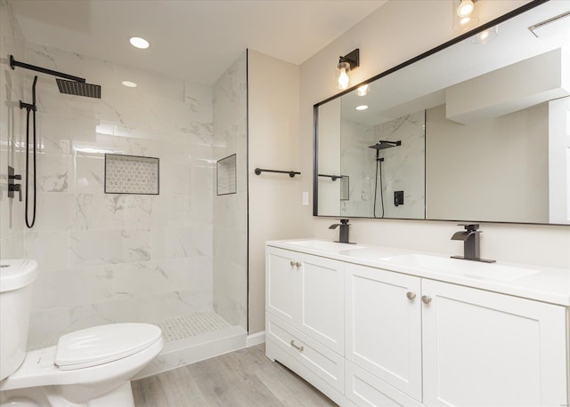 bathroom featuring toilet, a tile shower, hardwood / wood-style flooring, and vanity