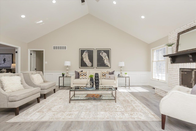 living room featuring vaulted ceiling, a brick fireplace, and hardwood / wood-style floors