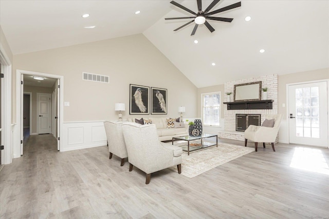 living room with ceiling fan, light hardwood / wood-style floors, a fireplace, and high vaulted ceiling