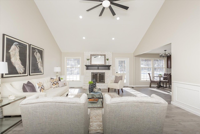 living room with high vaulted ceiling, wood-type flooring, ceiling fan with notable chandelier, and a fireplace