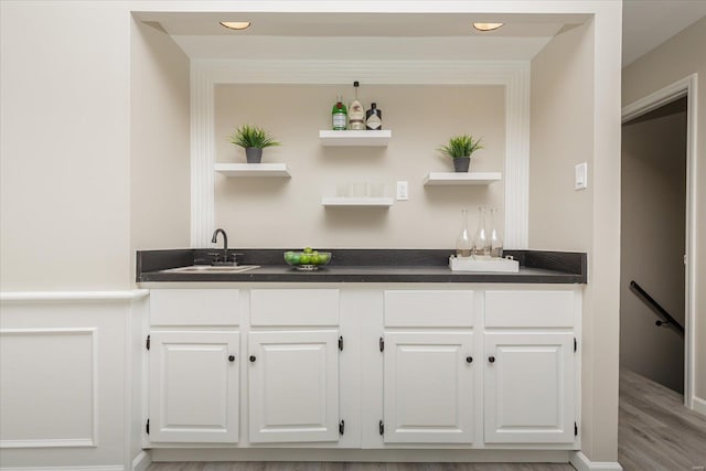 bar featuring light hardwood / wood-style floors, sink, and white cabinetry