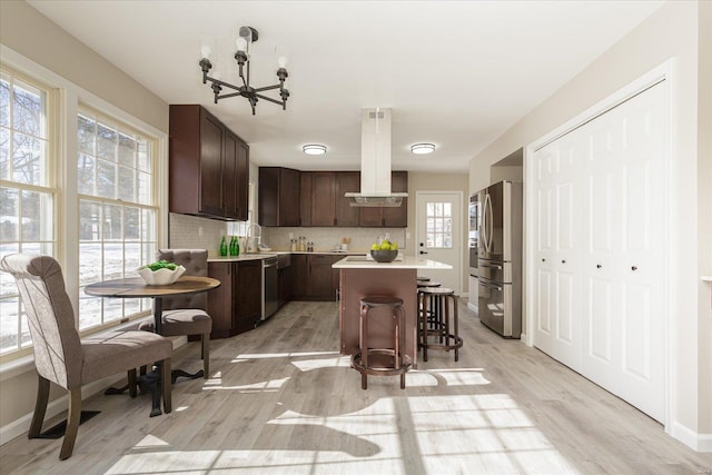 kitchen with island range hood, a kitchen bar, stainless steel appliances, a kitchen island, and dark brown cabinetry