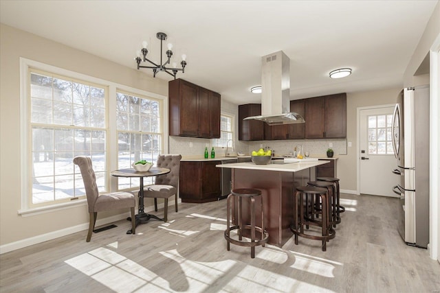 kitchen with light hardwood / wood-style floors, island range hood, stainless steel fridge, dark brown cabinets, and a center island