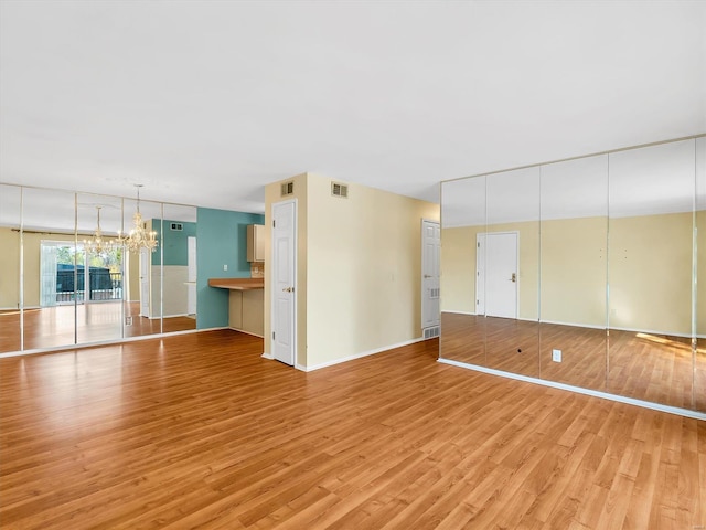 unfurnished living room with an inviting chandelier and light hardwood / wood-style flooring