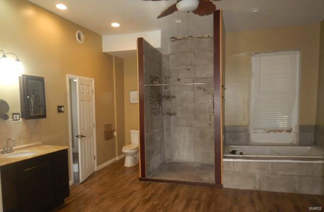 bathroom with wood-type flooring, tiled tub, vanity, toilet, and ceiling fan