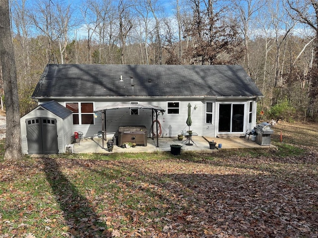 rear view of house with a hot tub, a storage unit, and a patio