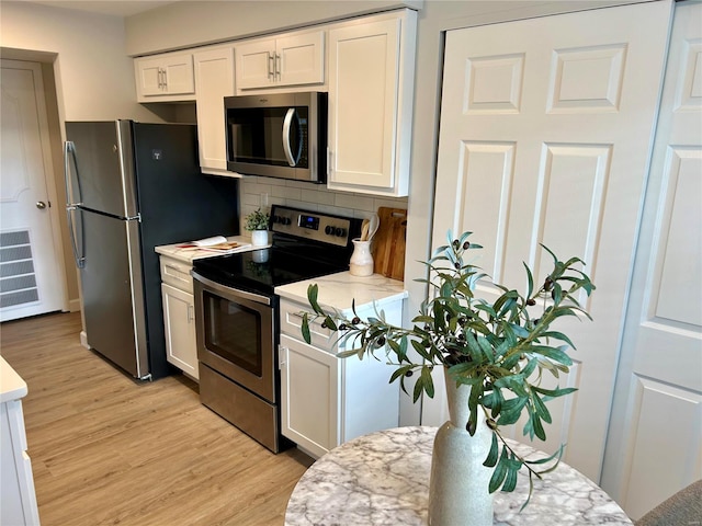 kitchen featuring appliances with stainless steel finishes, backsplash, light hardwood / wood-style floors, and white cabinetry