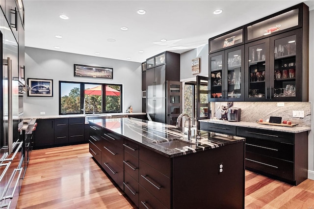 kitchen featuring an island with sink, light hardwood / wood-style floors, stainless steel appliances, and light stone counters