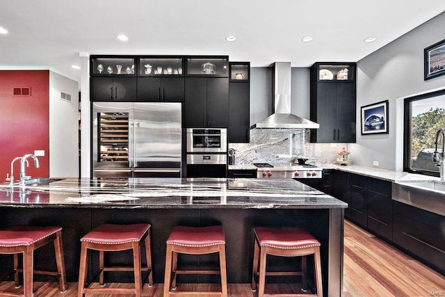 kitchen featuring appliances with stainless steel finishes, a kitchen bar, a kitchen island, wall chimney range hood, and light wood-type flooring