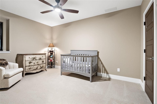 carpeted bedroom featuring a nursery area and ceiling fan