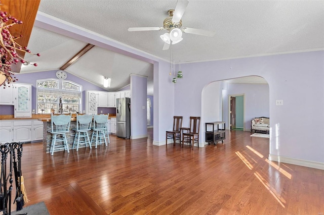 dining area featuring a textured ceiling, lofted ceiling with beams, ceiling fan, and dark wood-type flooring