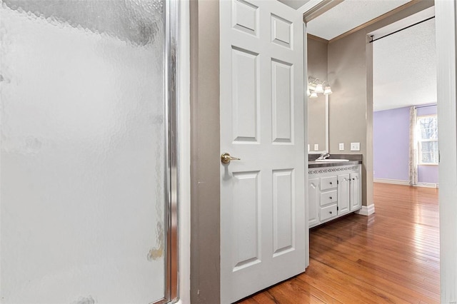 bathroom featuring a textured ceiling, vanity, wood-type flooring, and a shower with door