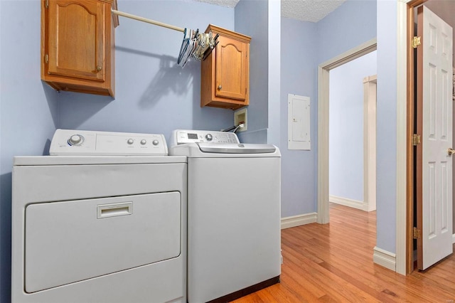 laundry room with cabinets, a textured ceiling, washer and dryer, light hardwood / wood-style flooring, and electric panel