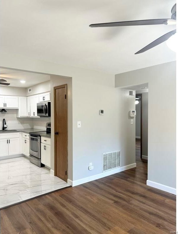 kitchen with backsplash, sink, light wood-type flooring, appliances with stainless steel finishes, and white cabinetry