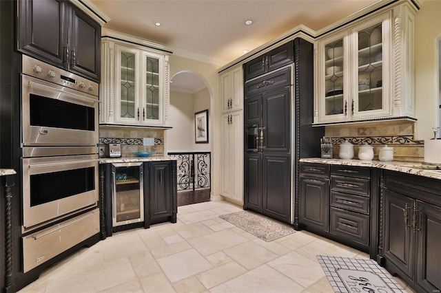 kitchen featuring light stone countertops, decorative backsplash, stainless steel double oven, crown molding, and wine cooler