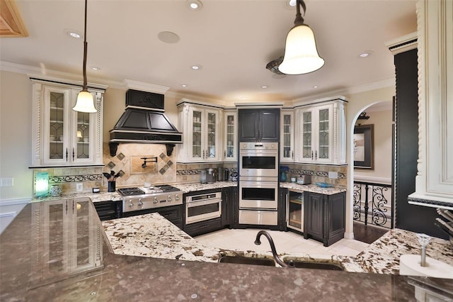 kitchen with sink, custom range hood, hanging light fixtures, and appliances with stainless steel finishes