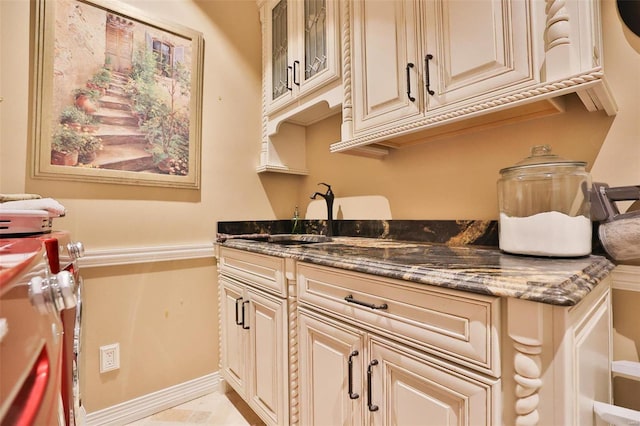 kitchen featuring cream cabinetry, dark stone countertops, and sink