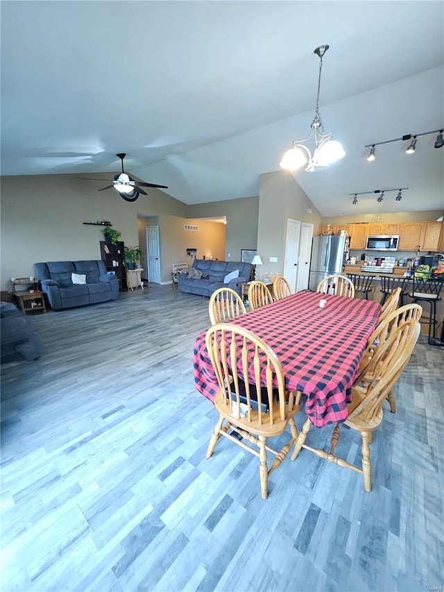 dining area with ceiling fan with notable chandelier, hardwood / wood-style flooring, and vaulted ceiling