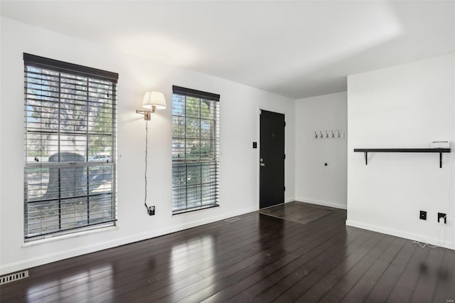 empty room with visible vents, baseboards, and dark wood-style flooring