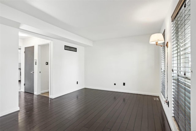 empty room featuring visible vents, dark wood-type flooring, and baseboards