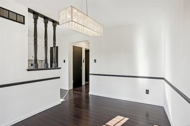 empty room with a notable chandelier, visible vents, baseboards, and hardwood / wood-style floors