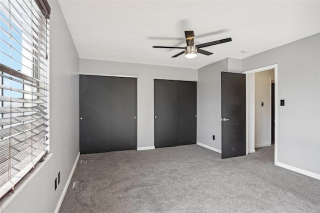 unfurnished bedroom featuring baseboards, multiple closets, carpet floors, and visible vents