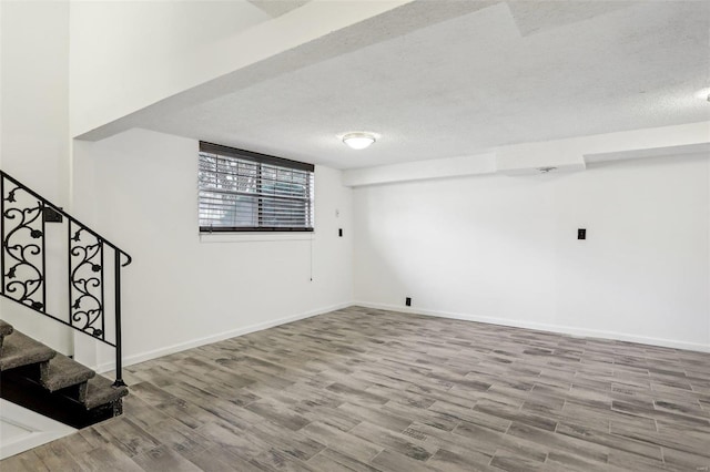 basement with stairway, a textured ceiling, baseboards, and wood finished floors