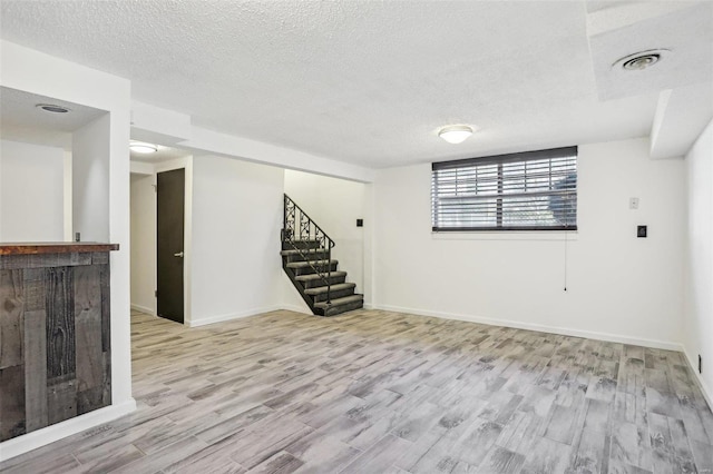 below grade area with visible vents, a textured ceiling, wood finished floors, baseboards, and stairs