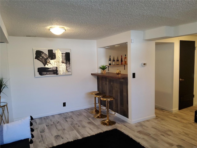 bar featuring a dry bar, a textured ceiling, baseboards, and wood finished floors