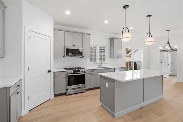 kitchen with stainless steel appliances, gray cabinets, pendant lighting, sink, and light hardwood / wood-style floors