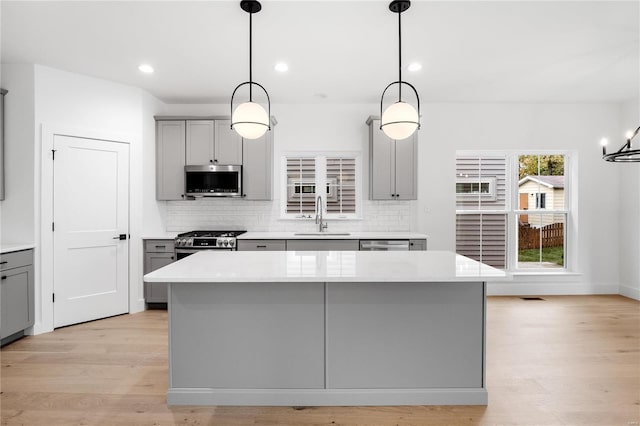 kitchen featuring stainless steel appliances, a kitchen island, gray cabinets, pendant lighting, and sink