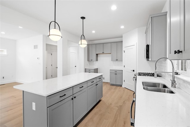 kitchen featuring light hardwood / wood-style floors, sink, gray cabinetry, a kitchen island, and decorative light fixtures