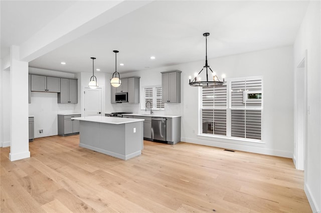 kitchen featuring hanging light fixtures, light hardwood / wood-style floors, appliances with stainless steel finishes, and a kitchen island