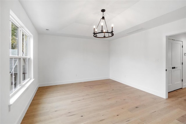 empty room featuring light hardwood / wood-style floors, a notable chandelier, and a raised ceiling