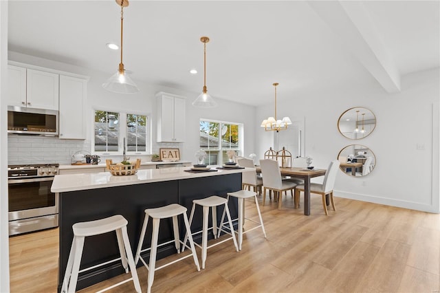 kitchen featuring white cabinets, decorative light fixtures, appliances with stainless steel finishes, and light hardwood / wood-style flooring