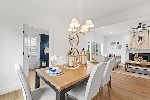 dining room featuring a premium fireplace, light hardwood / wood-style floors, and ceiling fan with notable chandelier