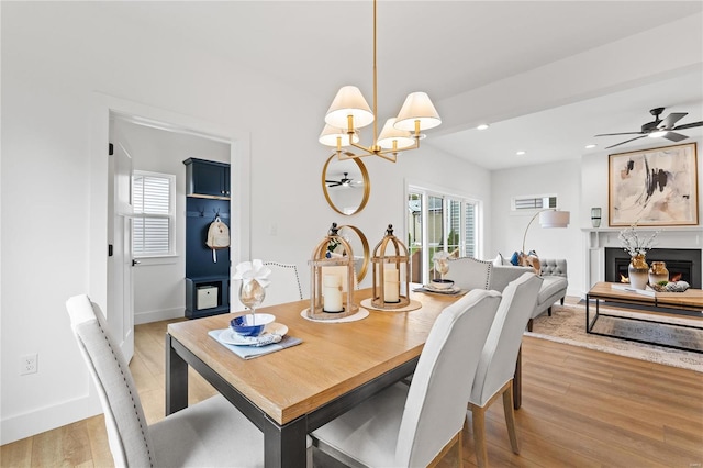 dining room with ceiling fan with notable chandelier, light hardwood / wood-style floors, and a fireplace