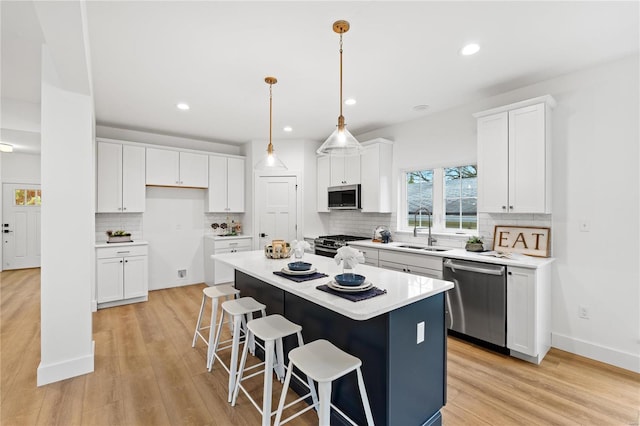 kitchen featuring appliances with stainless steel finishes, sink, a center island, light hardwood / wood-style floors, and white cabinetry