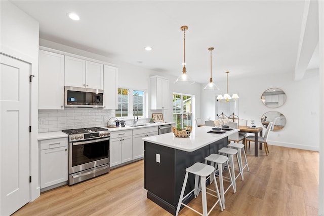 kitchen with appliances with stainless steel finishes, light hardwood / wood-style flooring, white cabinets, a kitchen island, and hanging light fixtures